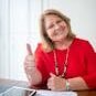 Happy senior woman wearing glasses gives a thumbs up in a red shirt, displaying positivity.